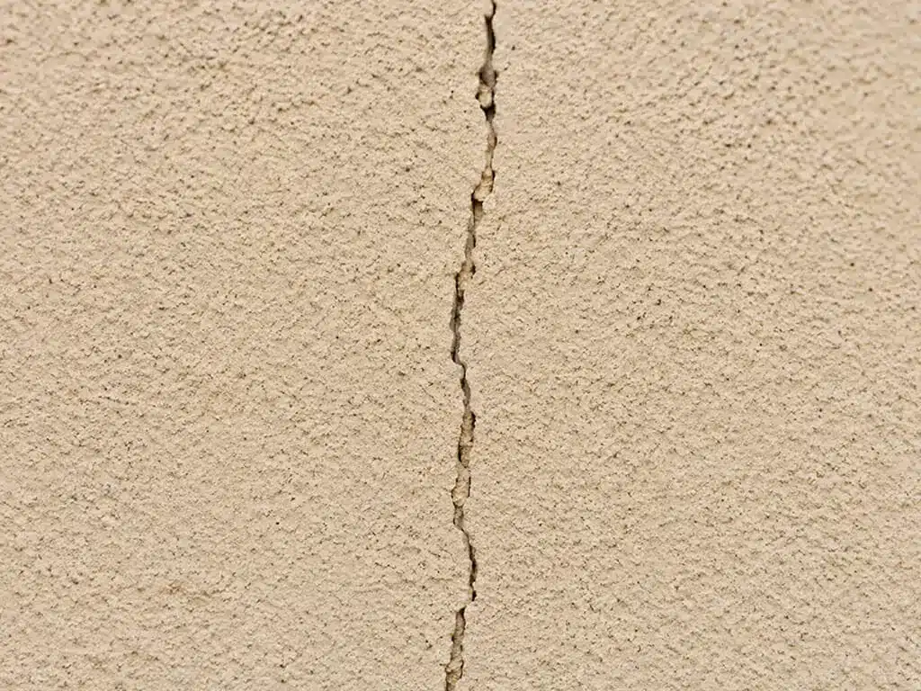 Fissure fine verticale traversant l'enduit d'un mur